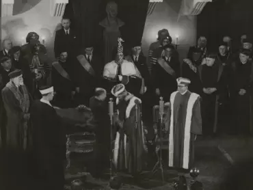 Ministr školství a osvěty prof. JUDr. Jaroslav Stránský uvádí 21. února 1947 rektora UP v Olomouci prof. PhDr. Josefa Ludvíka Fischera do úřadu zavěšením rektorského řetězu na šíji. Archiv UP v Olomouci.